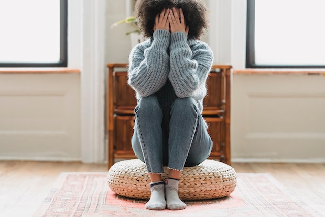 woman sitting in a pillow on the grown putting her hands over her face.